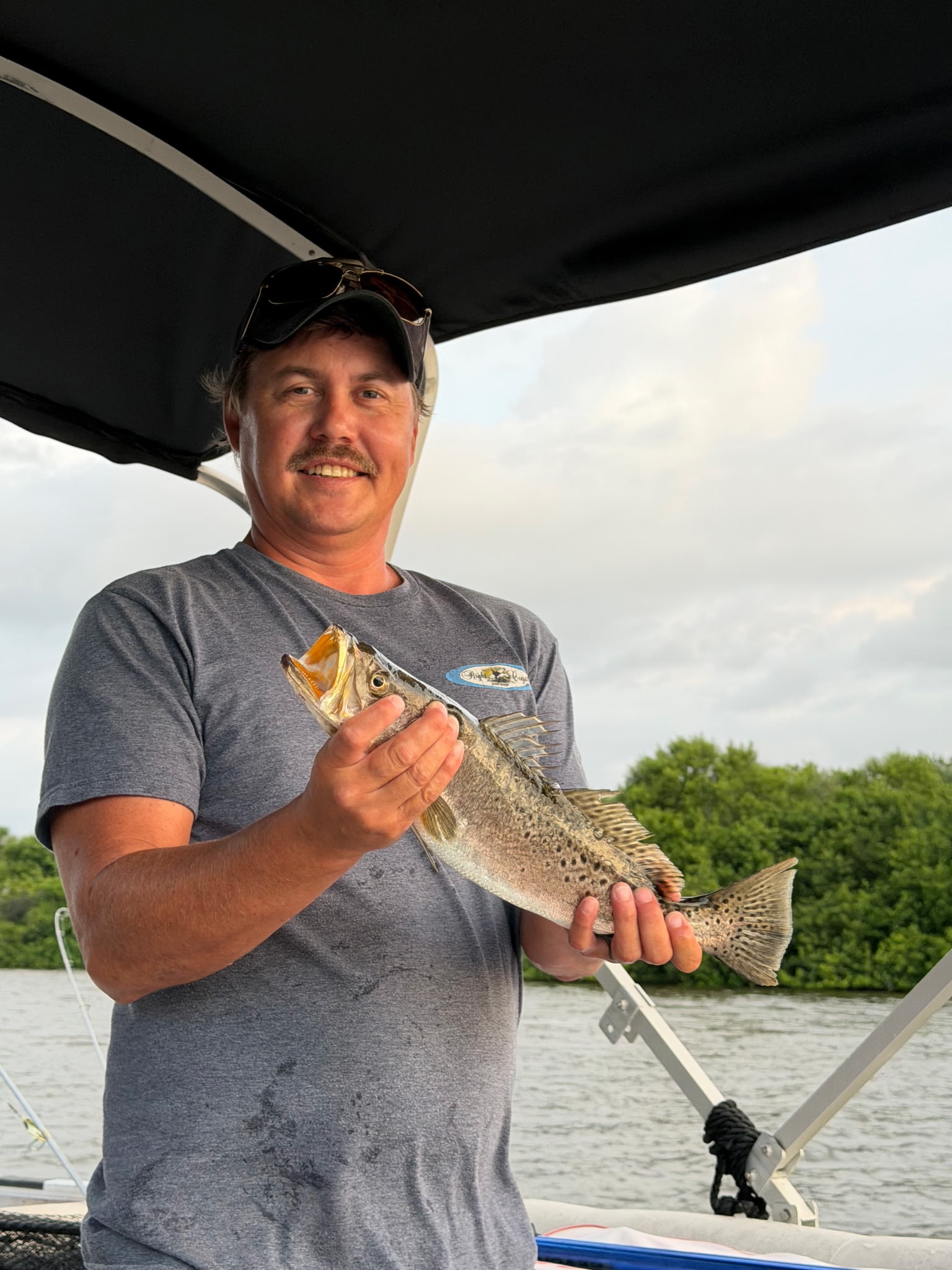 Angler holding a speckled trout caught on the Indian River Lagoon with mangroves in the background